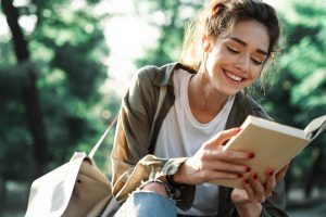 Image of attractive woman smiling and reading book in green park